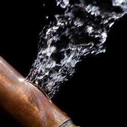 A bursting copper pipe in Gloucester, with water gushing out.